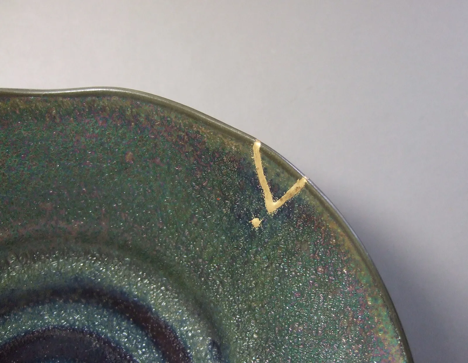 Close-up of a dark green glazed plate whose chipped rim has been filled with gold.