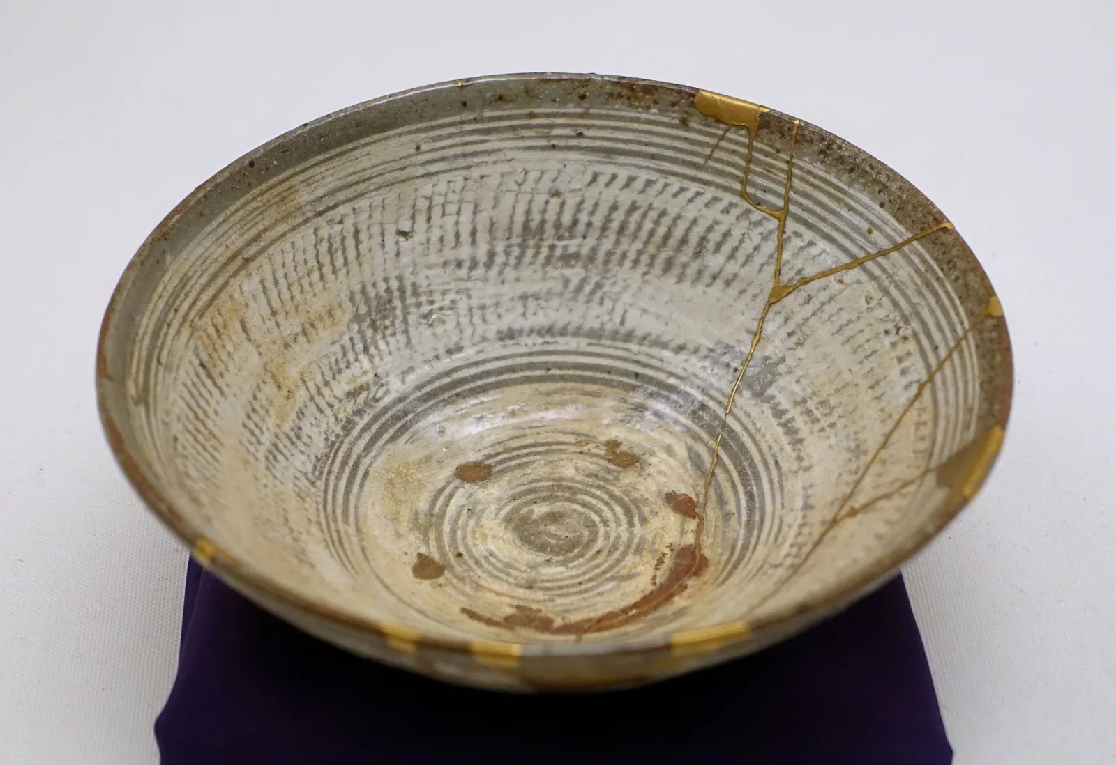 A sixteenth-century Korean stoneware tea bowl with combed white rings, its cracks and chipped rim repaired with gold lacquer.